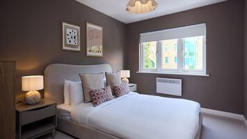 A bedroom with a bed, bedside tables, wall art, a window, and a ceiling light fixture.