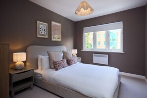A bedroom with a bed, bedside tables, wall art, a window, and a ceiling light fixture. - Oak & Earth Isle of Dogs Apartment (London)