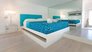 Ein modernes Schlafzimmer mit einem großen Bett, einem Nachttisch mit Lampe und einem großen Spiegel.