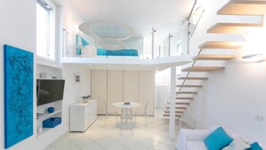 Ein modernes Interieur mit Essbereich, einer Couch mit blauen Kissen, einer Treppe und einem Fernseher auf einem weißen Schrank.