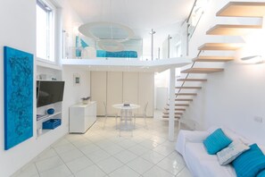 A modern interior with a dining area, a sofa with blue cushions, a staircase, and a TV on a white cabinet. - Rooftop Luxury Apartment (Capri)