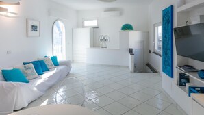 Ein modernes Wohnzimmer mit einem weißen Sofa, einem Fernseher und einem Essbereich mit einer weißen Kommode und einer blauen Vase.