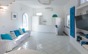 A modern living room with a white sofa, a TV, and a dining area with a white cabinet and a blue vase. - Rooftop Luxury Apartment (Capri)