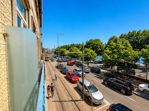 Eine Straße mit Straßenbahnschienen, parkenden Autos und einem Fußweg entlang eines Gebäudes mit einer verzierten Fassade.