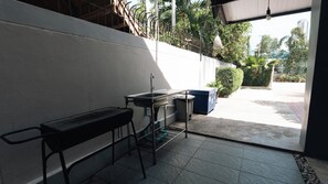 Una pequeña cocina al aire libre con un lavamanos, un banco y un cubo de basura.
