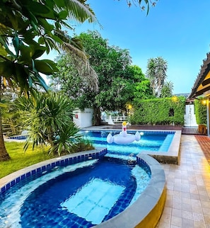 Una piscina con hidromasaje, rodeada de abundante vegetación y un sendero empedrado.