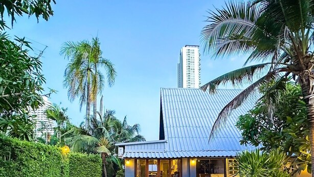 A swimming pool with a swan float, surrounded by lush greenery and a building with a tiled roof. - PAPA Beach Pool Villas Pattaya (Bang Lamung District)