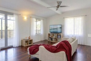 A living room with a sofa, a television, a bookshelf, and a ceiling fan. - Zen Outback Pool - Garden - Balcony - Parking (Darwin)