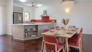 A modern kitchen with a central island, dining table with chairs, ceiling fans, and a window.