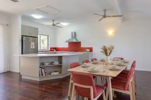 A modern kitchen with a central island, dining table with chairs, ceiling fans, and a window. - Zen Outback Pool - Garden - Balcony - Parking (Darwin)