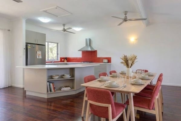 A modern kitchen with a central island, dining table with chairs, ceiling fans, and a window. - Zen Outback Pool - Garden - Balcony - Parking (Darwin)