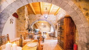 A stone-walled dining area with a wooden table set for a meal, a fireplace, and a wooden cabinet. - Traditional Villas Askyfou (Askyfou)