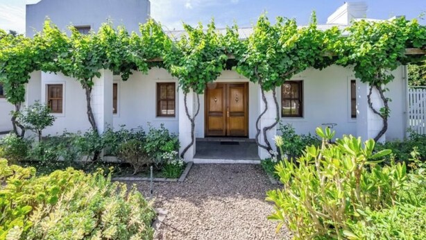 A white building with a wooden door and windows, surrounded by greenery and a gravel path. - Dream Holiday Home in the Heart of Franschhoek (Franschhoek)