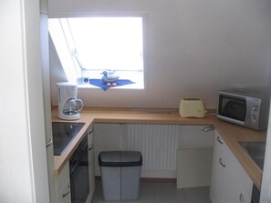 Eine kleine Küchenzeile mit Fenster, inklusive Toaster, Mikrowelle, Kaffeemaschine und Mülleimer.