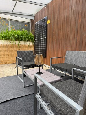 An outdoor seating area with metal-framed chairs and a table, a solar panel, and a wooden wall. - The Cozy Bad Ems Apartment (Bad Ems)