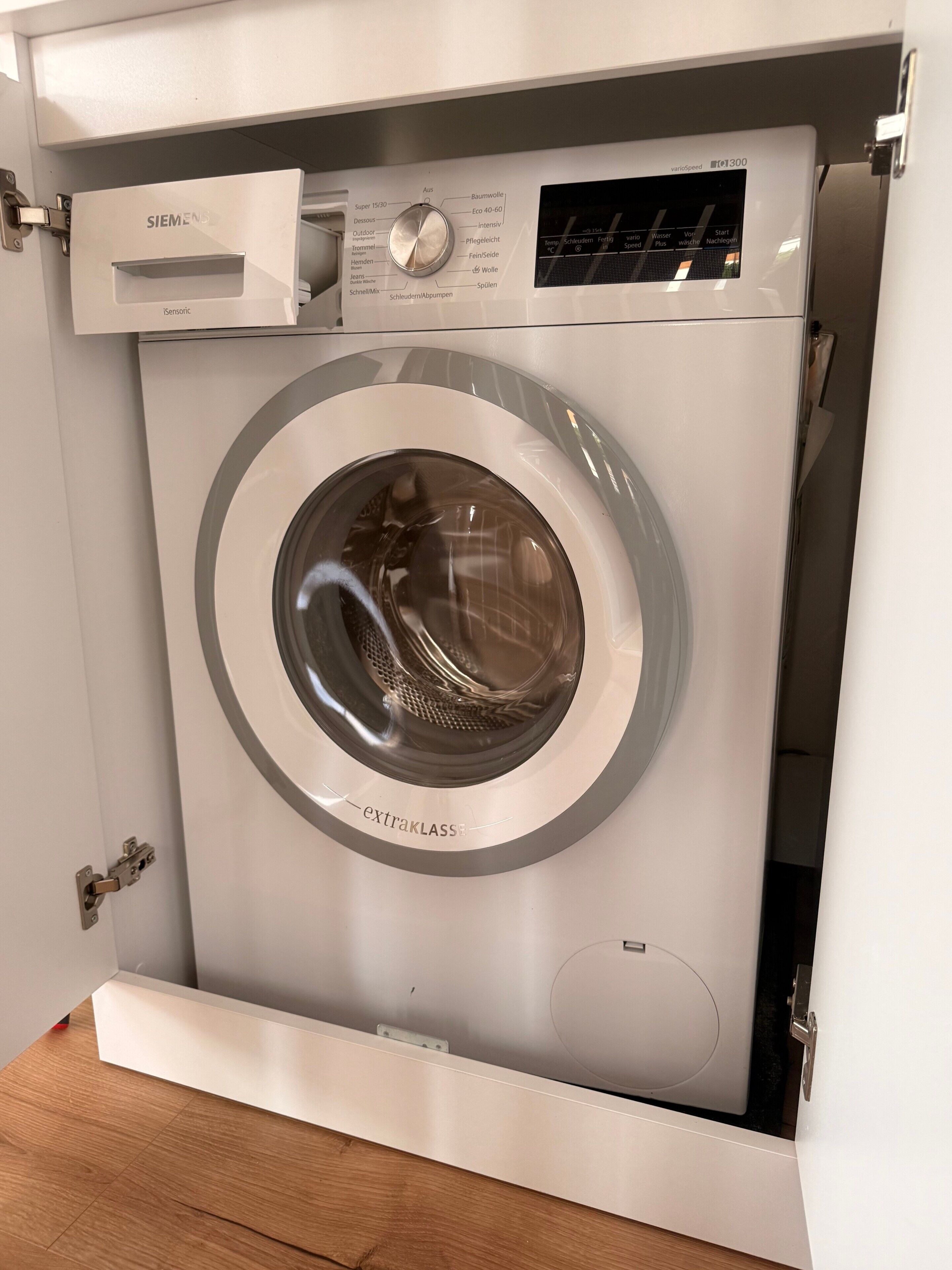 Eine Waschmaschine mit Frontlader, Bedienfeld und sichtbarem Wasseranschluss.