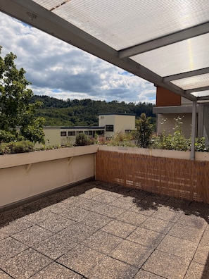 A rooftop terrace with a view of a forested hill, a building with a flat roof, and a pergola structure. - The Cozy Bad Ems Apartment (Bad Ems)