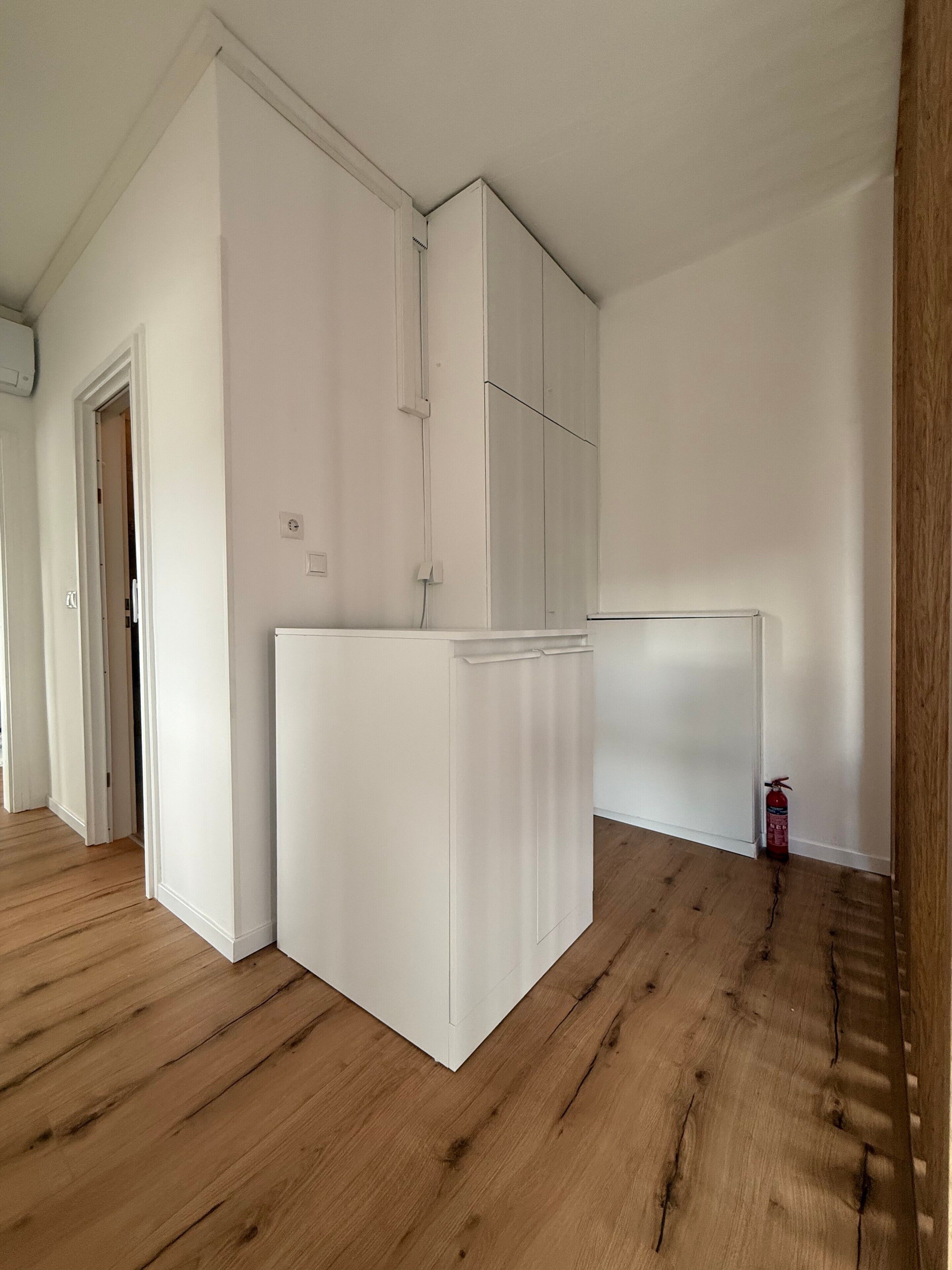 A room with a wooden floor, white walls, and a white built-in cabinet.
