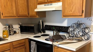 A kitchen with wooden cabinets, a microwave, stove, and various kitchen items. - Cozy 1-bedroom apartment with AC in serene Farmington Hills (Farmington Hills)