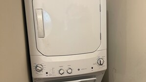 A front-loading washing machine with a control panel, a yellow energy guide sticker, and a wall-mounted dryer. - Cozy 1-bedroom apartment with AC in serene Farmington Hills (Farmington Hills)