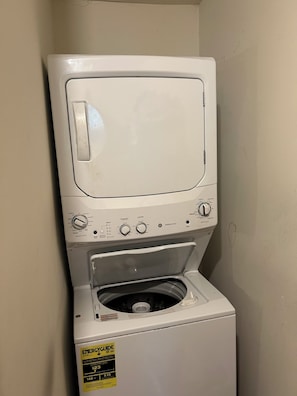 Eine Waschmaschine mit Frontlader, einer gelben Energieeffizienzaufklebersowie ein an der Wand befestigter Trockner.