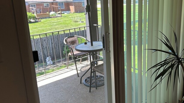 A balcony with a table and chairs, a potted plant, and a view of a grassy yard and a building. - Cozy 1-bedroom apartment with AC in serene Farmington Hills (Farmington Hills)