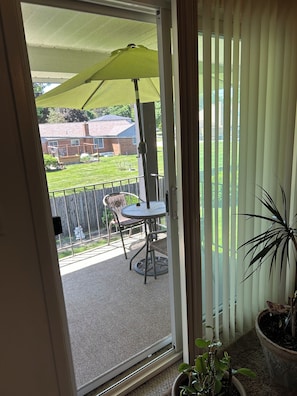 Een balkon met een tafel, stoelen, een bloempot en uitzicht op een gazon en een gebouw.