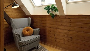 Un sillón de estampado pata de gallo con un cojín marrón, una lámpara de pie negra, una pared de madera, una planta en maceta y un tragaluz.