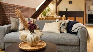 Una sala de estar con un sofá gris, un florero con plantas secas y una mesa de centro de madera.