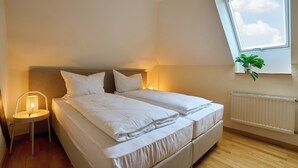 Un dormitorio con cama, lámpara de noche, ventana, radiador y una planta.
