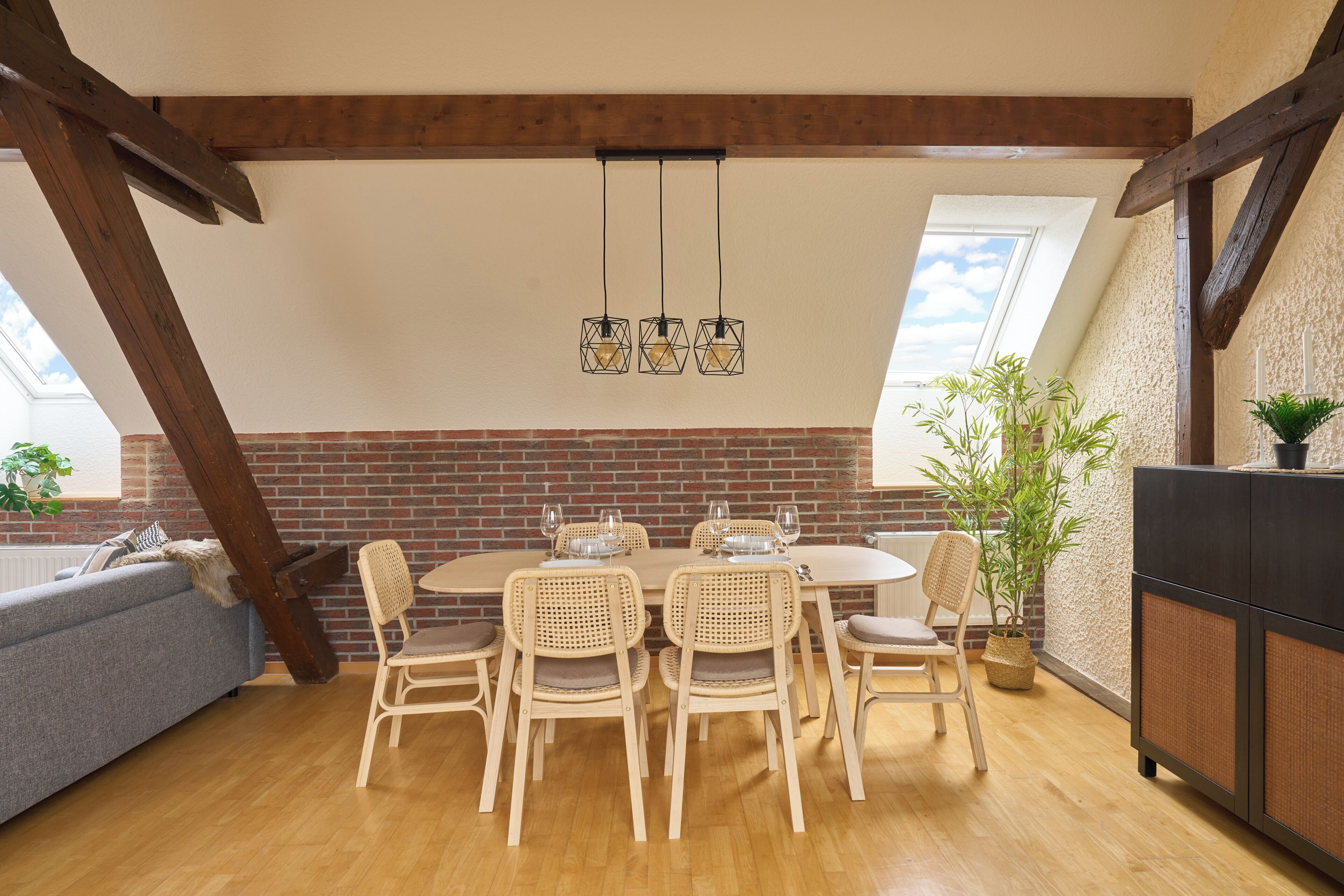 Ein Essbereich mit Backsteinwand, Holzbalkendecke, einem runden Tisch mit Stühlen und hängenden Pendelleuchten.