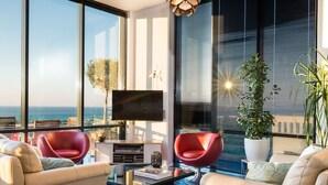 Ein modernes Wohnzimmer mit großem Fernseher, zwei roten Sesseln, einer Couch und einem Couchtisch mit Büchern.
