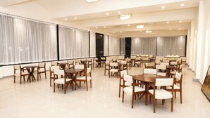 Un comedor espacioso con varias mesas y sillas, ventanas amplias con cortinas y suelo pulido.