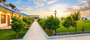 A pathway leading to a building with a blue roof, surrounded by greenery and a lamp post. - Vanam hotel and resort (Mathura)