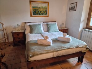 Una cama bien hecha con una colcha verde y blanca, dos almohadas y dos toallas dobladas sobre la cama.