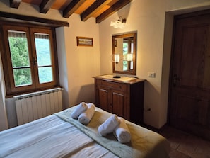 Ein Schlafzimmer mit einem Bett, einer hölzernen Kommode, einem Spiegel, einem Fenster mit Jalousien und einer Heizung.