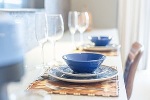Ein Esstisch ist gedeckt mit blauen Schüsseln, klaren Weinfässern und Besteck auf gewebten Platzsets.