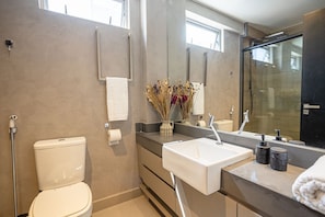 Ein modernes Badezimmer mit Toilette, Waschbecken, Dusche und einem großen Spiegel.