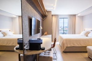 Ein modernes Hotelzimmer mit zwei Betten, einem großen Spiegel, einem runden Tisch mit einer Kaffeemaschine und Blick auf die Stadt.