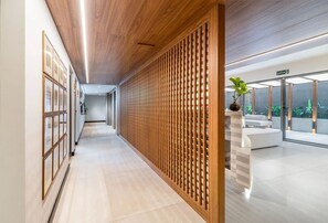 A hallway with a wooden slat partition, a white sofa, and a potted plant. - Way Bossa #J5 - Apartamento en Bessa by Carpediem (João Pessoa)