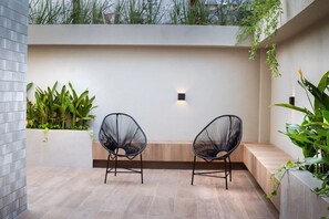 A modern outdoor seating area with two black chairs, a light wall, and green plants. - Way Bossa #J5 - Apartamento en Bessa by Carpediem (João Pessoa)