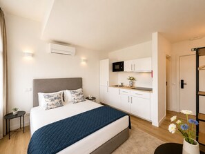 Ein modernes Hotelzimmer mit Bett, Küchenzeile und einer Tür zu einem weiteren Raum.