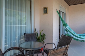 Un patio con mobiliario de mimbre, una mesa de vidrio, una hamaca y una planta en maceta.