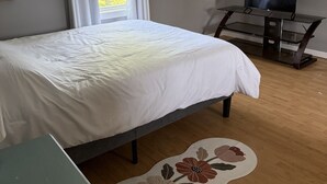 A bedroom with a bed, a TV on a stand, a window with curtains, and a wooden floor. - Tata Tides Getaway (Tatamagouche)