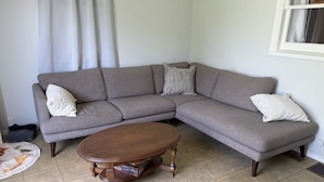 A living room with a grey sectional sofa, two white pillows, a round wooden coffee table, and a tiled floor. - Tata Tides Getaway (Tatamagouche)