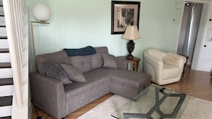 A living room with a grey sofa, a glass coffee table, a lamp, a framed picture on the wall, and a white chair. - Tata Tides Getaway (Tatamagouche)