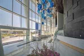 Eine großzügige Lobby mit großen Fenstern, einer modernen Treppe und einer dekorativen Glasdecke.