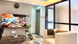 A modern living room with a flat-screen TV, a sofa, a coffee table, and a large window. - Shamm Goldpark homes 1bd (Nairobi)