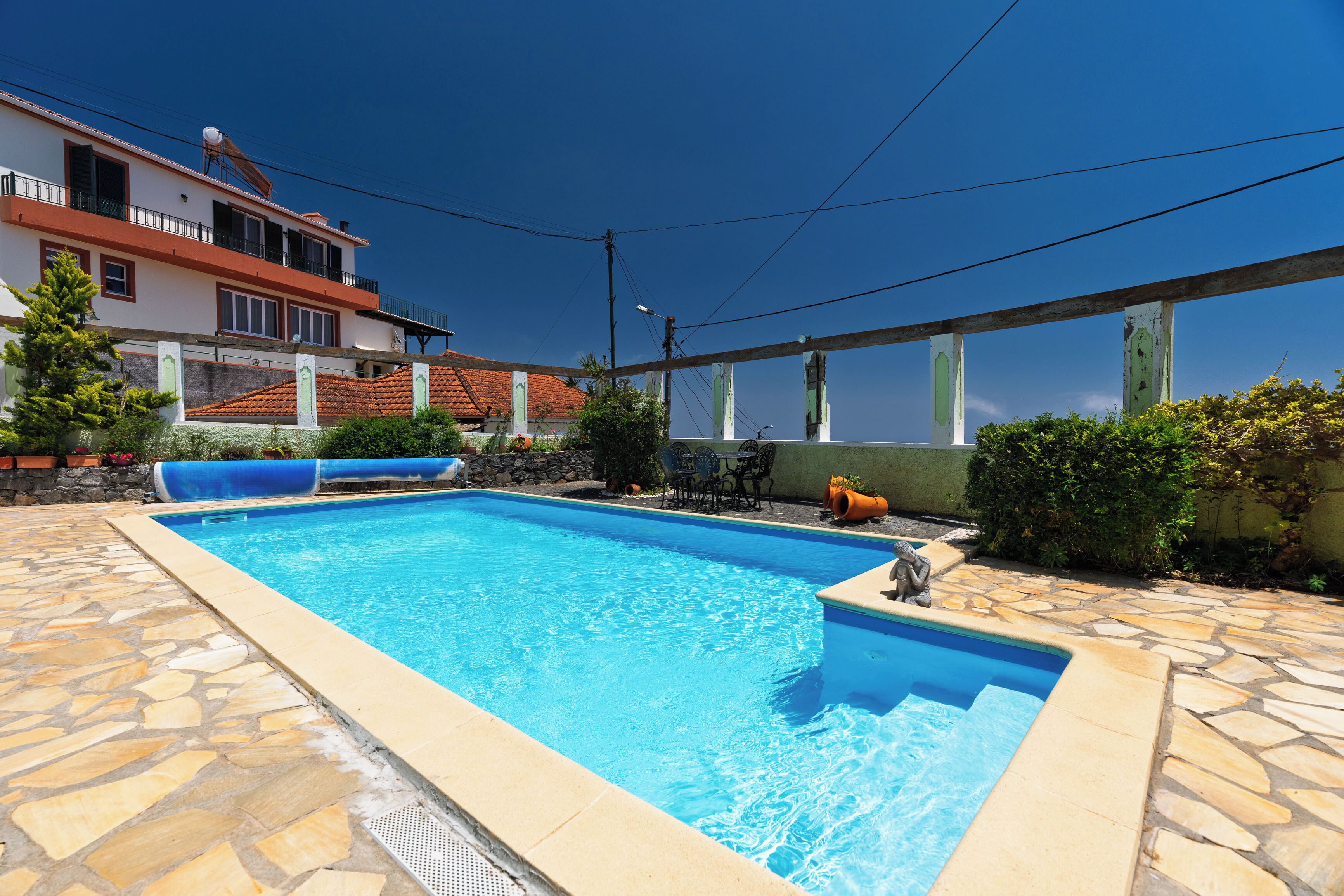 Una piscina rectangular con suelo de baldosas de piedra, un pequeño área de estar al aire libre y un edificio con balcones al fondo.