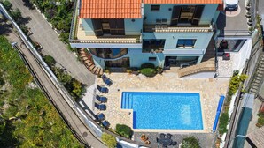 A two-story building with a swimming pool, outdoor seating, and a solar panel on the roof.